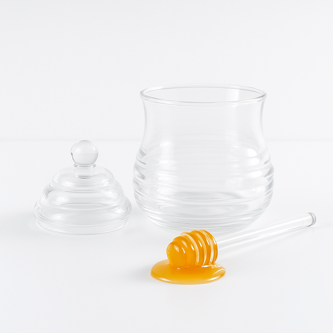 Clear glass honey jar with lid and honey dipper on a white background