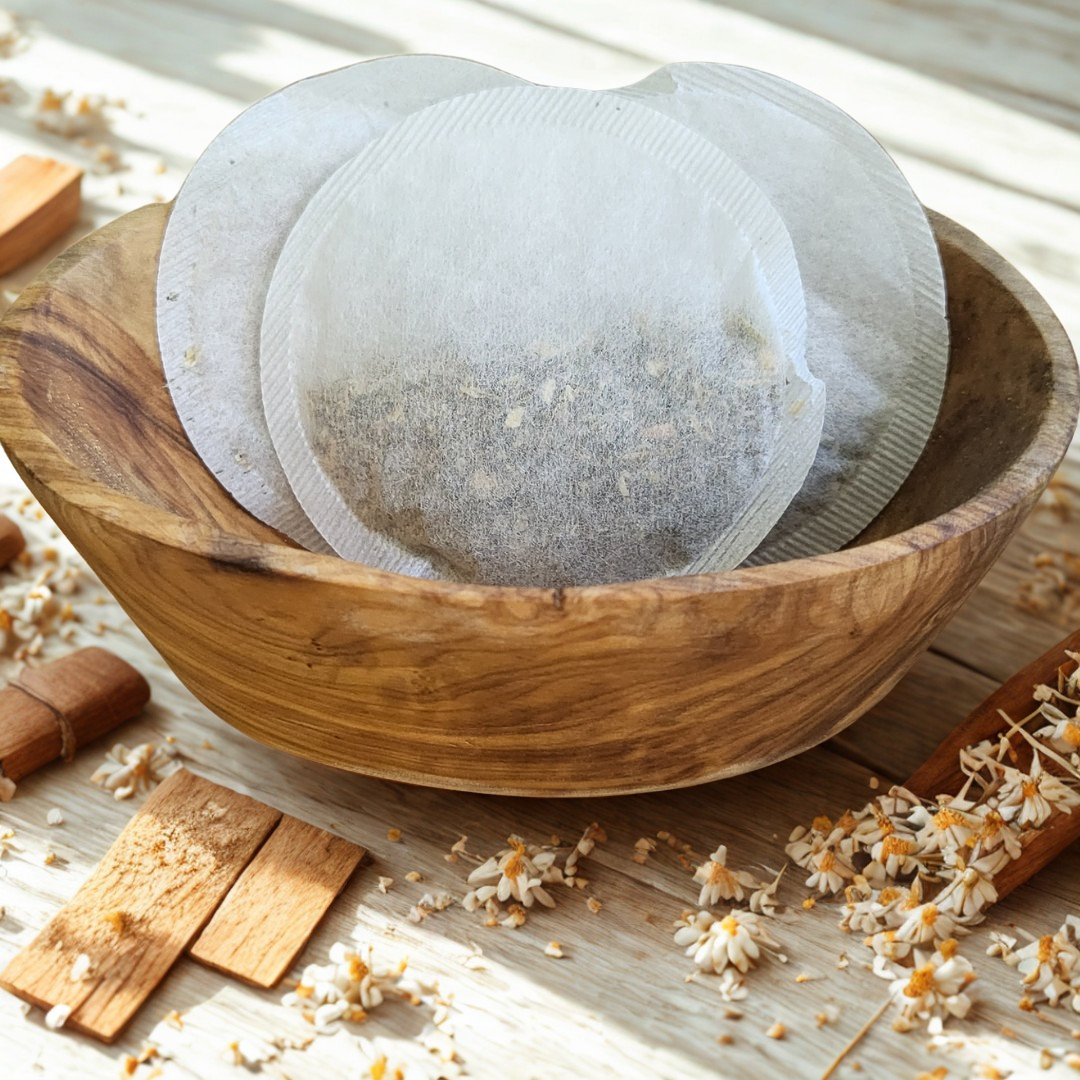 Wooden bowl with tea bags on a wooden surface with flowers and wood pieces.