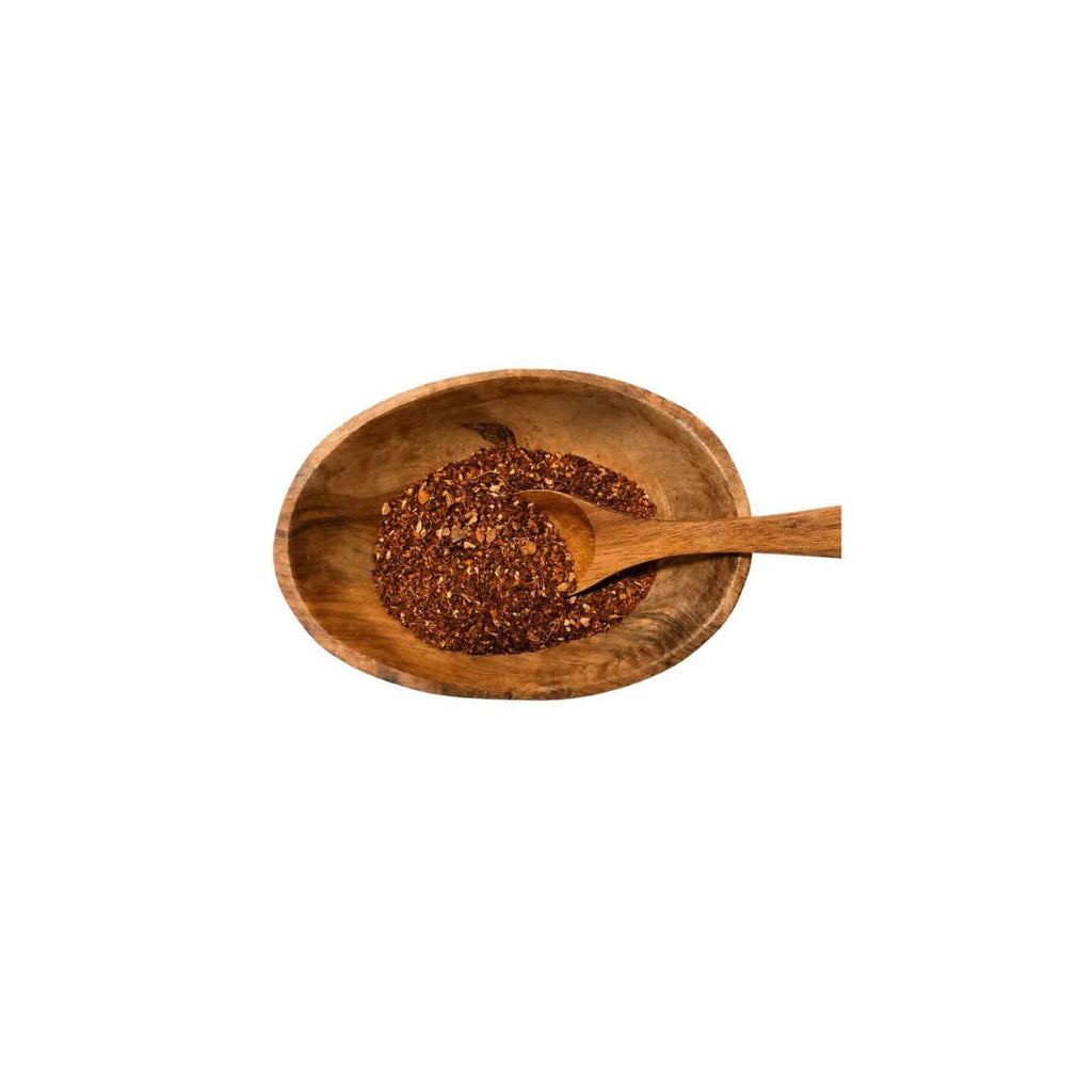 A small wooden bowl filled with reddish-brown ground spice or pepper flakes, with a wooden spoon resting inside, shown on a plain white background.