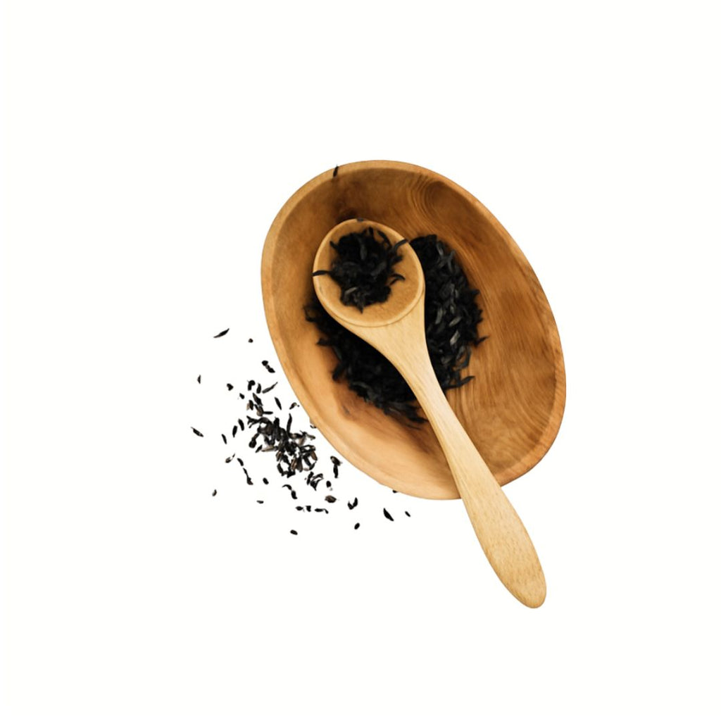 Wooden scoop and spoon with black tea leaves on a white background