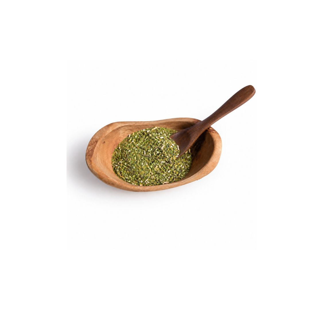 A small wooden bowl filled with chopped green herbs or tea, with a wooden spoon resting inside, photographed on a clean white background.
