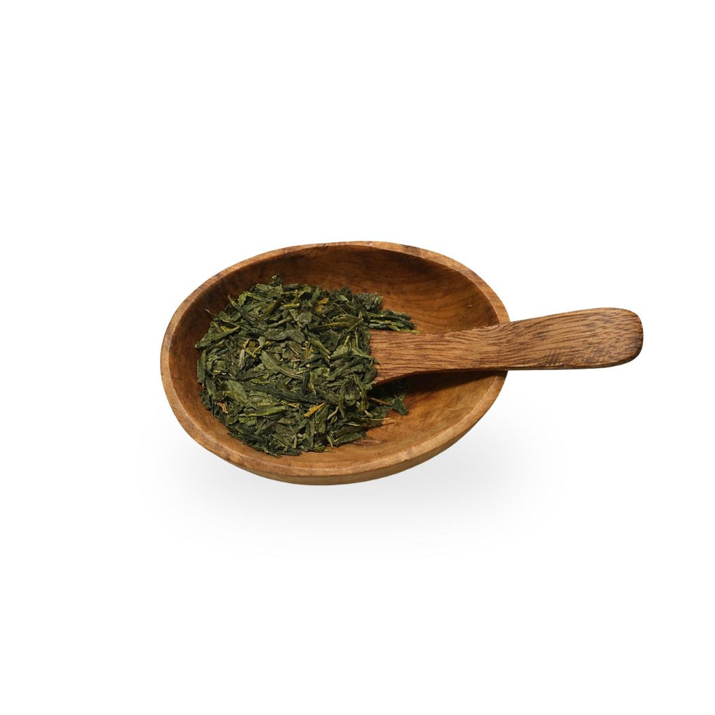 Wooden scoop with green tea leaves in a wooden bowl on a white background