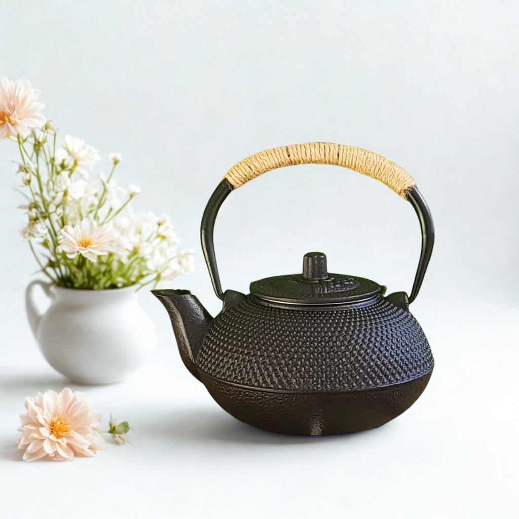 Black textured teapot with a wicker handle on a light background with flowers.