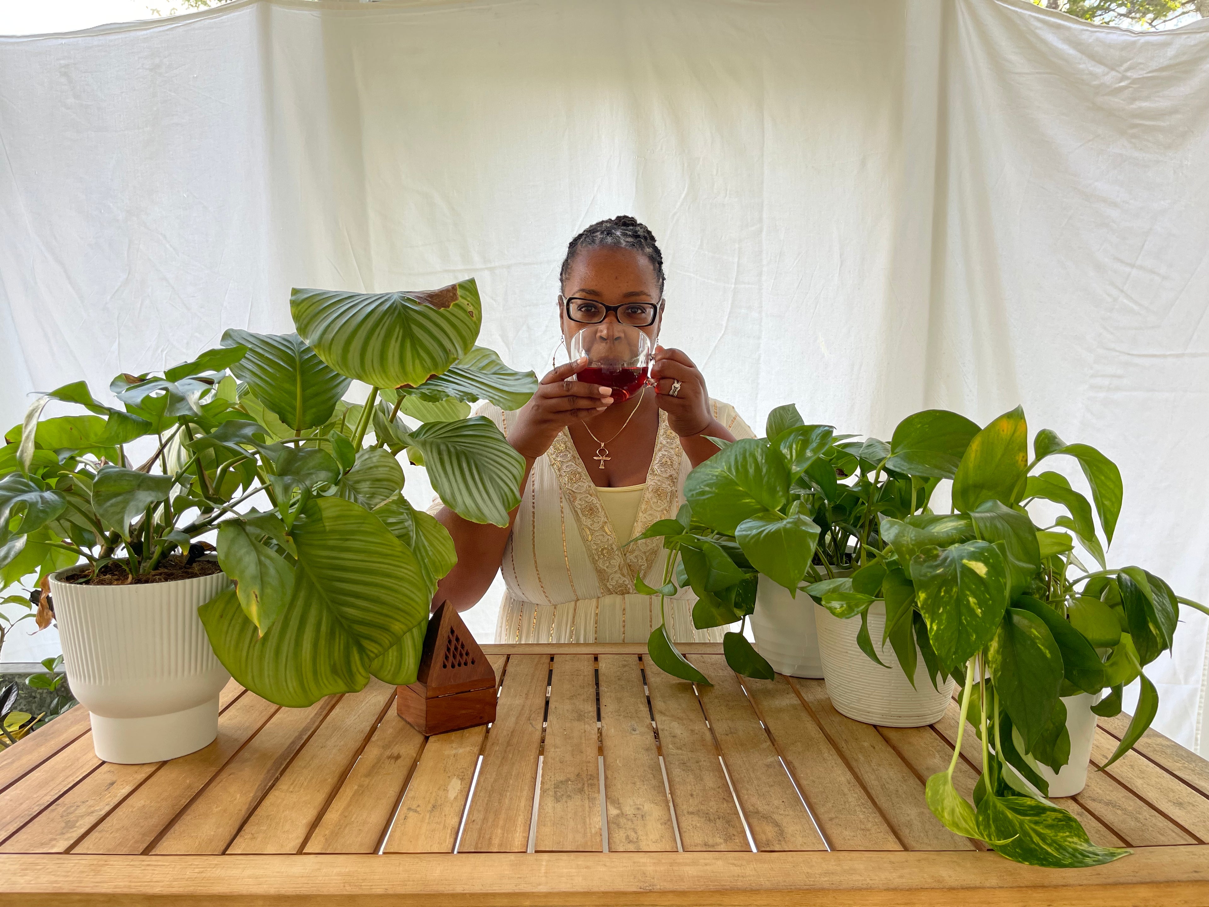 Woman sitting at a table with potted plants, drinking from a glass.