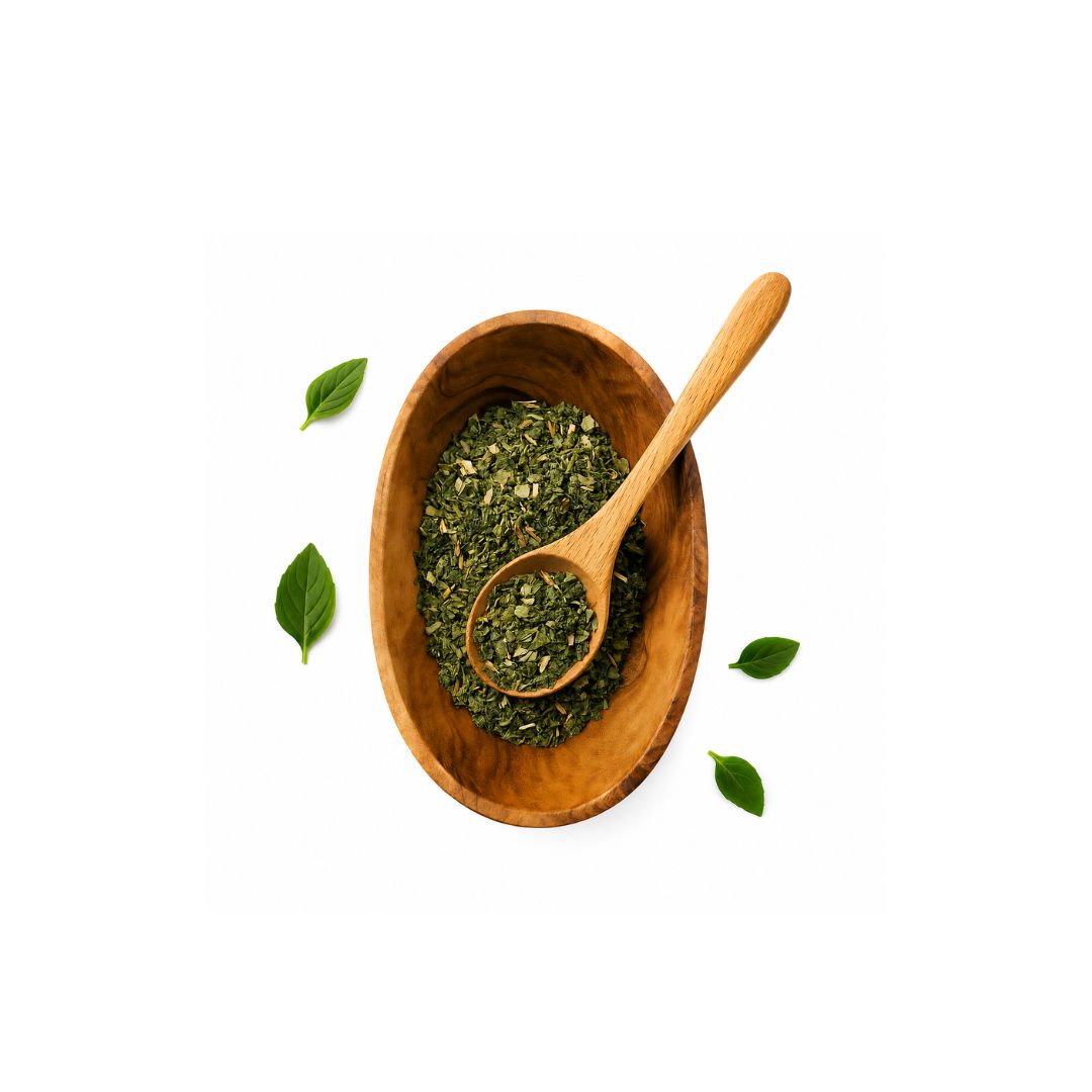 A top-down view of dried green tea leaves in a wooden bowl with a wooden spoon, surrounded by three scattered green leaves on a solid white background.