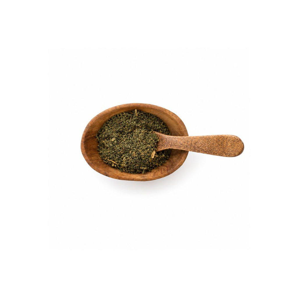 A small wooden spoon filled with dried green herbs or tea leaves, photographed from above on a plain white background.