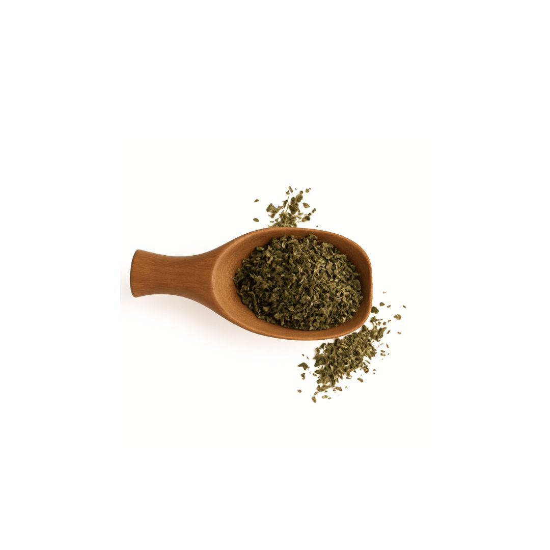 Dried green herbs or tea leaves in a small wooden spoon on a plain white background.