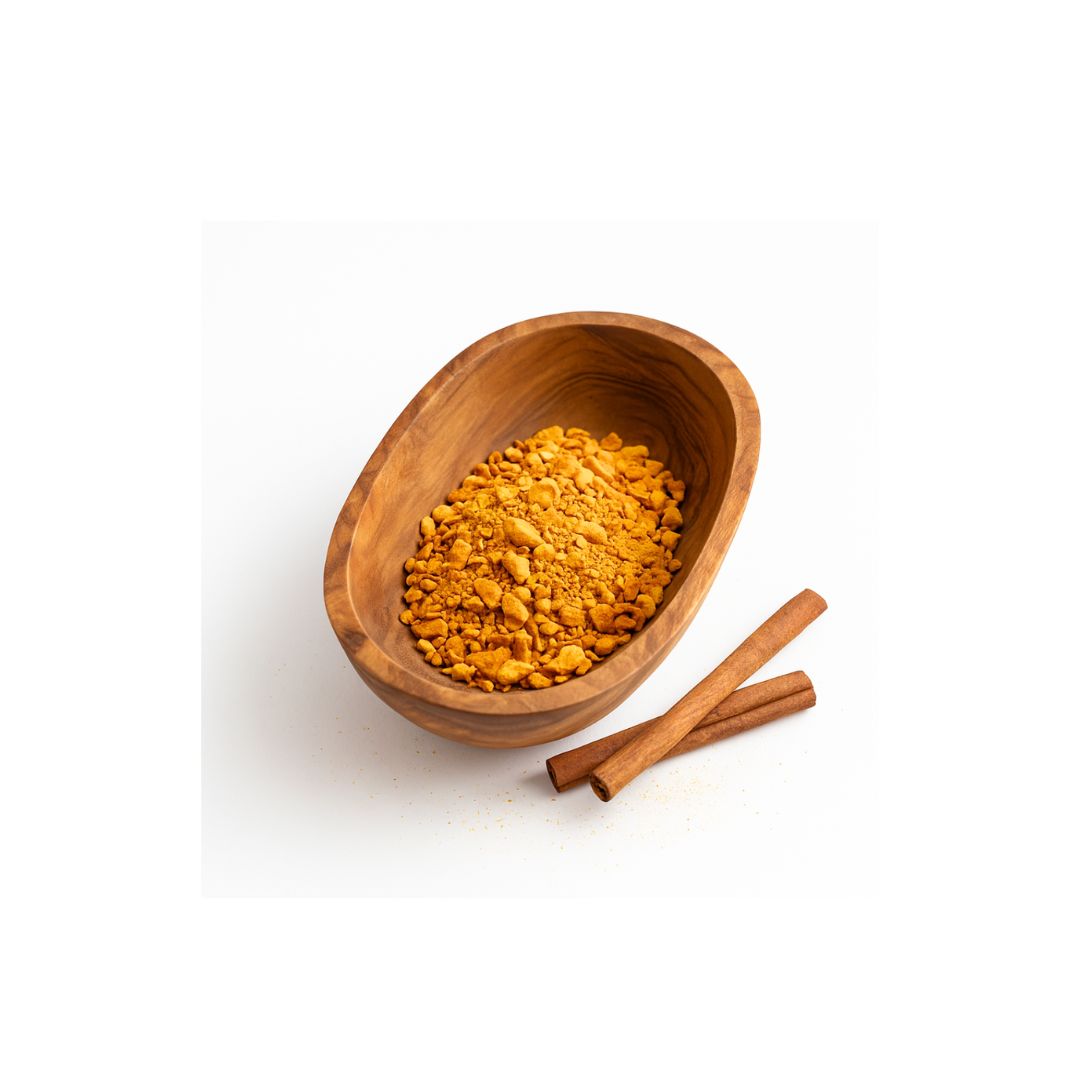 A small wooden bowl filled with a yellow-orange ground spice, with two cinnamon sticks beside it on a clean white background.