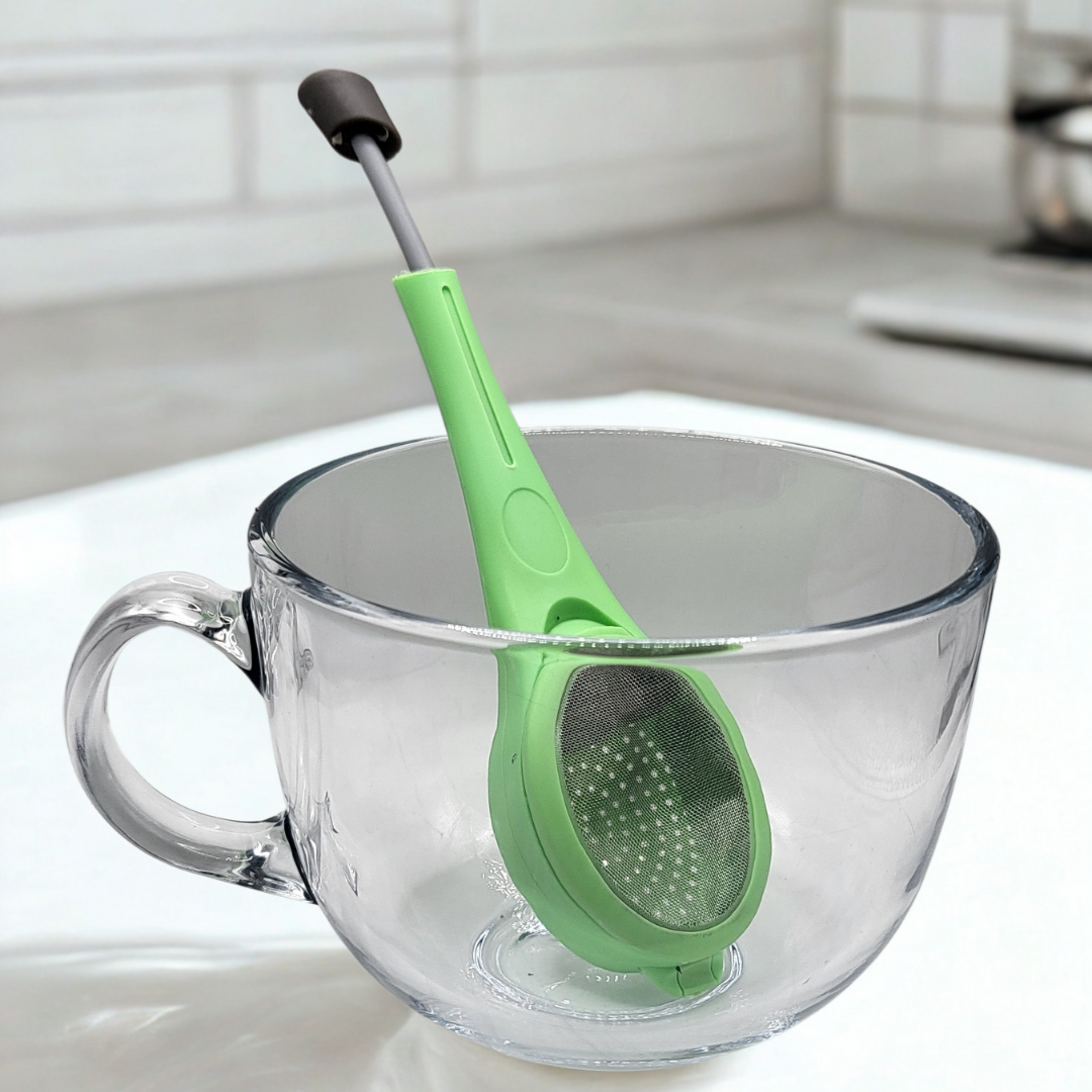Green tea infuser in a clear glass mug on a white surface