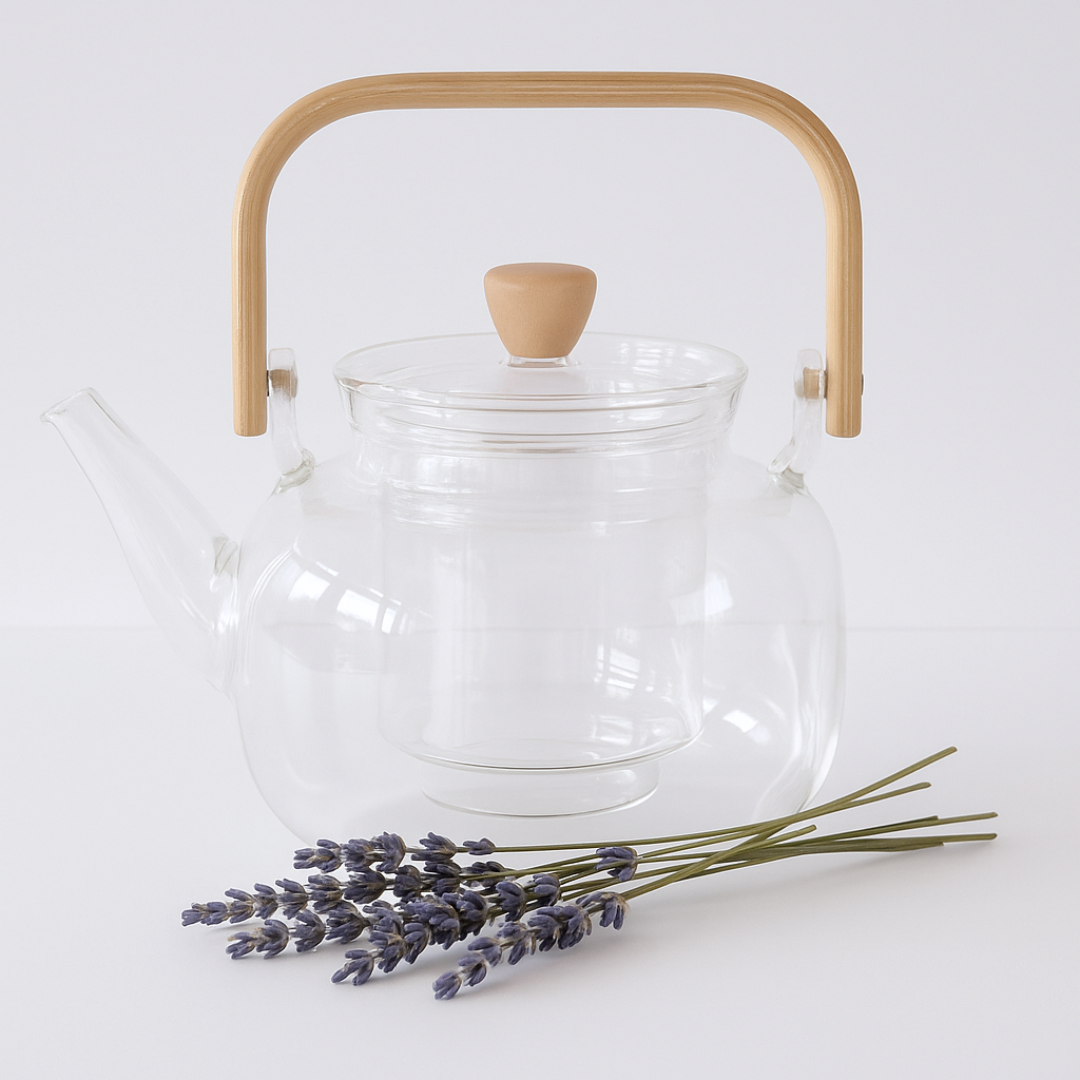 Clear glass teapot with wooden handle and lid on a white background with lavender flowers.