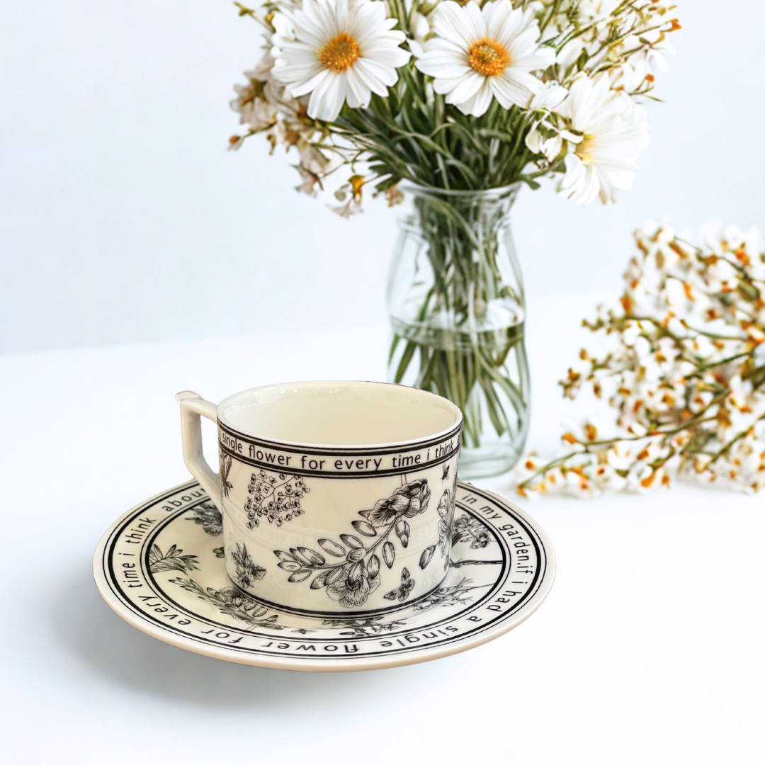 Ceramic cup and saucer with floral design on a white background with flowers.