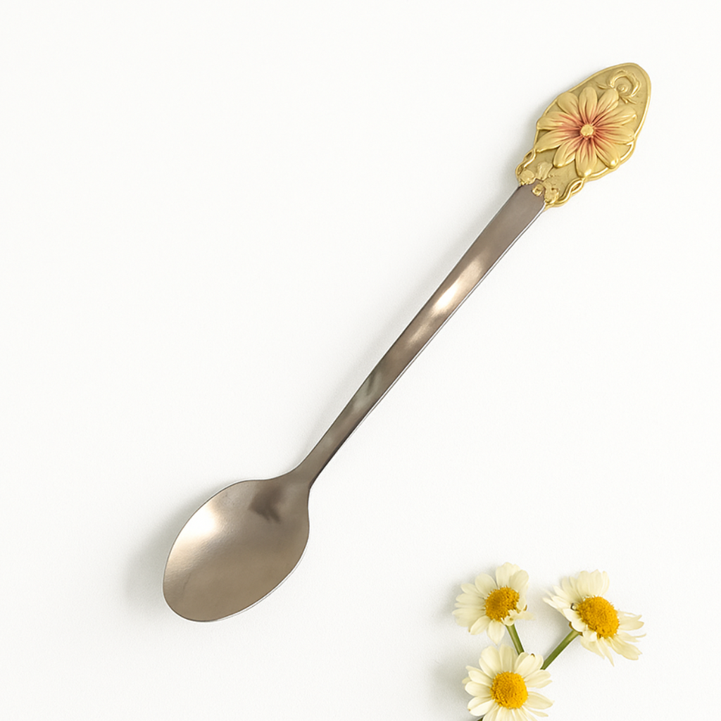 Decorative spoon with a gold handle featuring a floral design, placed on a white background with small flowers.