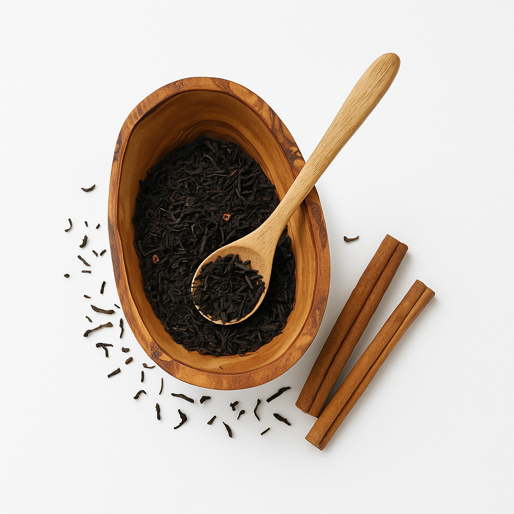 Wooden bowl with black tea leaves, a wooden spoon, and cinnamon sticks on a white background